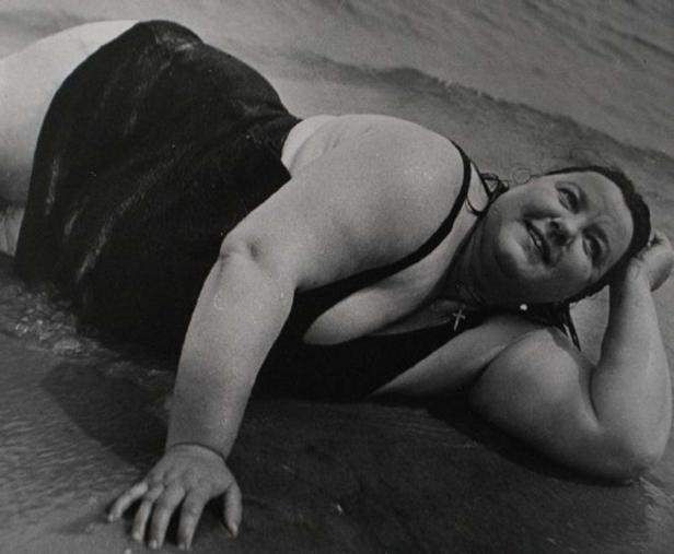 Eine Frau liegt im Badeanzug am Strand und lächelt.