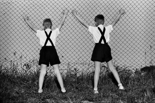 Zwei Jungen stehen mit dem Rücken zur Kamera an einem Zaun.