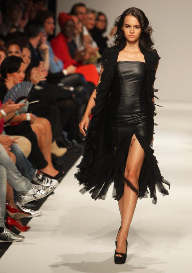 Eine Frau in einem schwarzen Kleid mit Fransen läuft über einen Laufsteg.