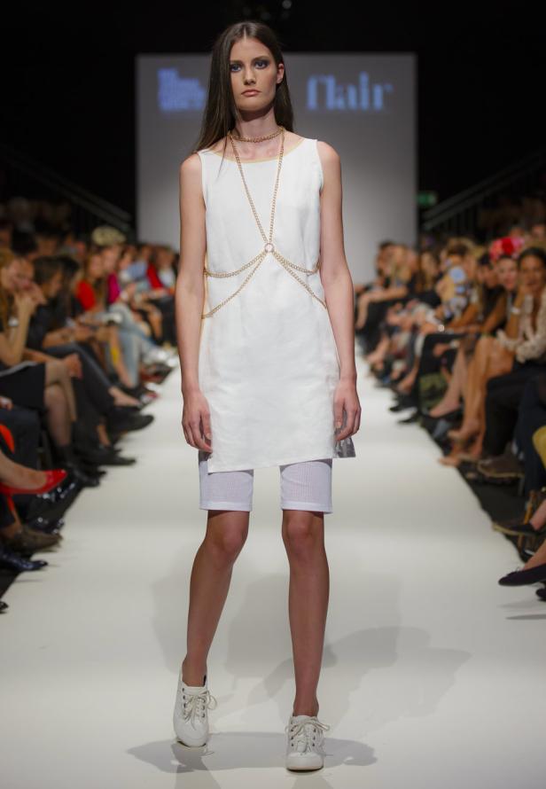 Eine Frau präsentiert ein weißes Kleid mit goldenen Ketten auf einem Laufsteg.