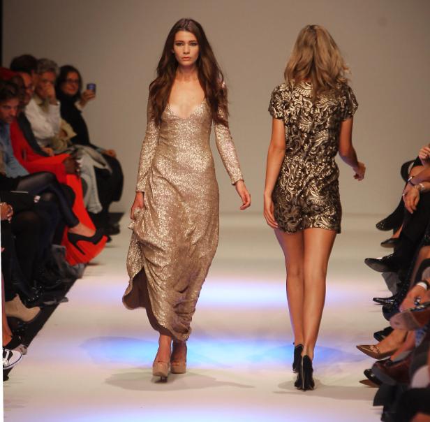 Zwei Models präsentieren goldene Kleider auf einem Laufsteg.