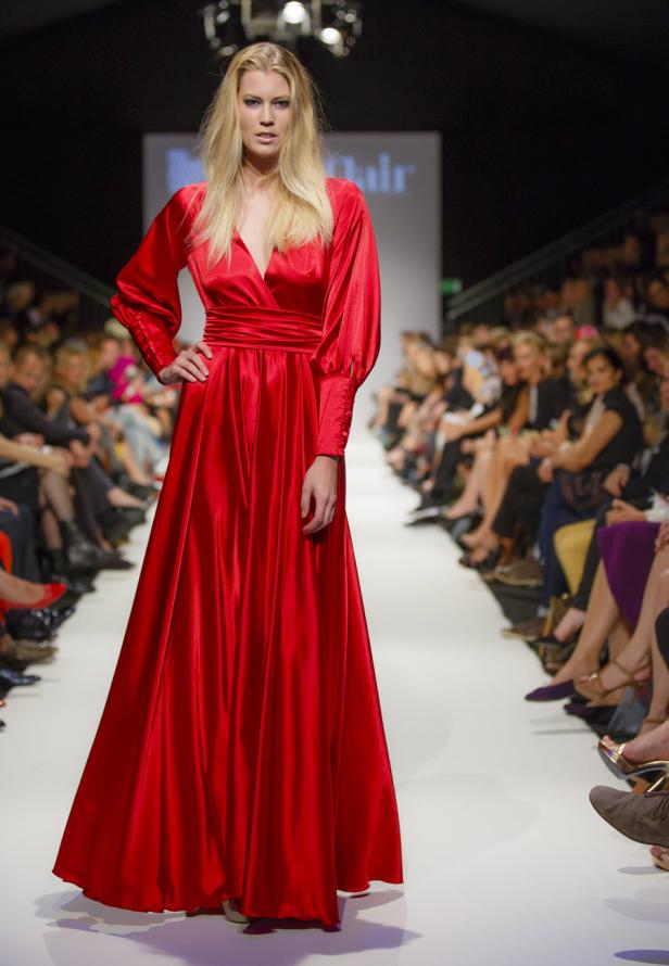 Eine blonde Frau in einem langen, roten Seidenkleid auf einem Laufsteg.