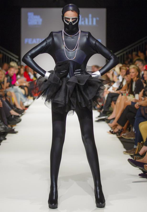 Eine Frau in einem schwarzen Ganzkörperanzug mit Tüllrock auf einem Laufsteg.