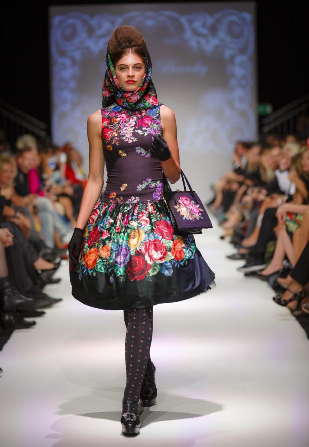 Eine Frau in einem floralen Kleid und Kopftuch läuft auf einem Laufsteg.