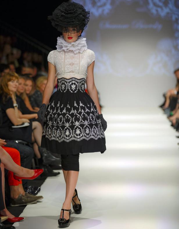 Eine Frau in einem schwarz-weißen Kleid mit Rüschenkragen läuft über einen Laufsteg.