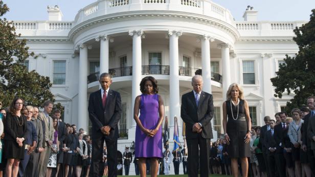 Barack Obama, Michelle Obama, Joe Biden und Jill Biden stehen mit gesenkten Köpfen vor dem Weißen Haus.