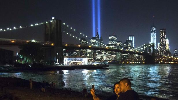 Ein Paar macht ein Selfie vor der Skyline von New York mit dem Tribute in Light und der Brooklyn Bridge.