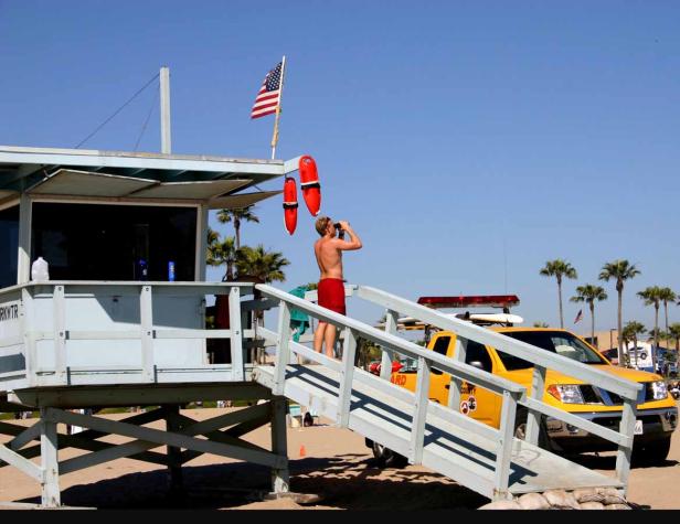 Ein Rettungsschwimmer beobachtet mit einem Fernglas den Strand von seinem Turm aus.