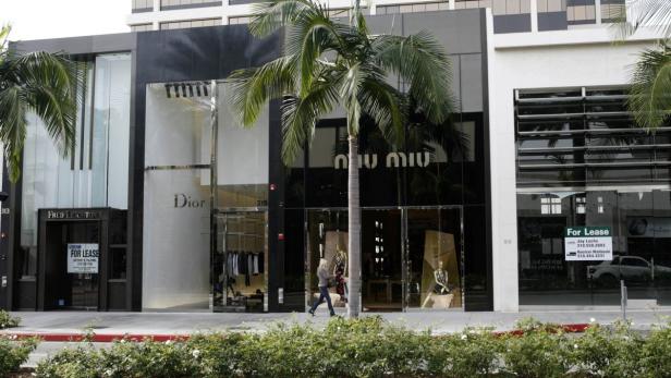 Blick auf eine Straße mit Geschäften wie Dior und Miu Miu, vor denen Palmen stehen.