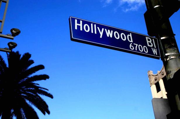 Ein blaues Straßenschild mit der Aufschrift „Hollywood BI 6700 W“ vor blauem Himmel.