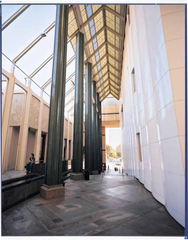 Eine Frau sitzt in der Eingangshalle eines Gebäudes mit hohen Säulen und Glasdach.