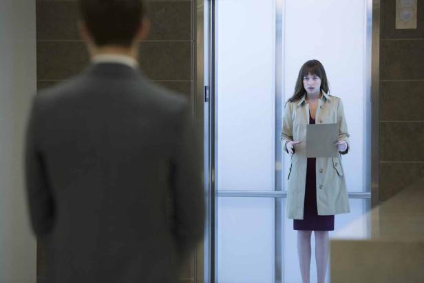 Dakota Johnson steht in einem Aufzug und hält einen Umschlag in der Hand.