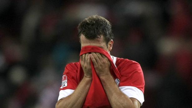 Ein Fußballspieler verdeckt sein Gesicht mit seinem roten Trikot.
