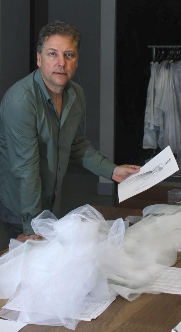 Ein Mann betrachtet eine Skizze eines Kleides, umgeben von Tüll auf einem Tisch.