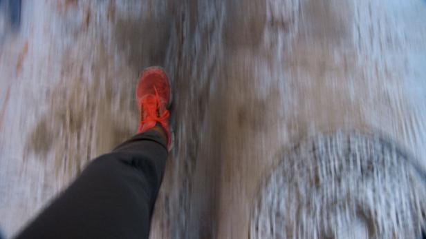 Ein Fuß mit einem roten Turnschuh auf einem unscharfen Untergrund.