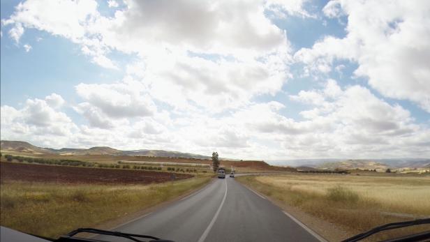 Blick aus einem fahrenden Auto auf eine Landstraße in ländlicher Umgebung.