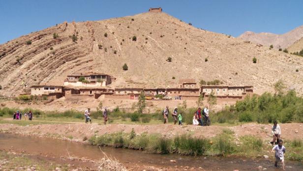 Eine Gruppe von Menschen wandert entlang eines Flusses in einer marokkanischen Landschaft.