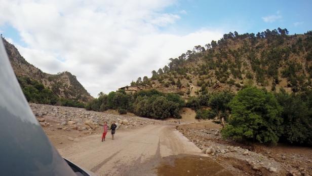 Zwei Kinder gehen auf einer Straße in einer bergigen Landschaft entlang.