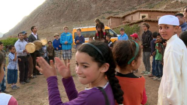 Eine Gruppe von Kindern und Erwachsenen versammelt sich in einem Dorf in Marokko.