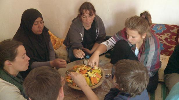 Eine Gruppe von Menschen isst gemeinsam aus einer großen Schüssel mit Gemüse.