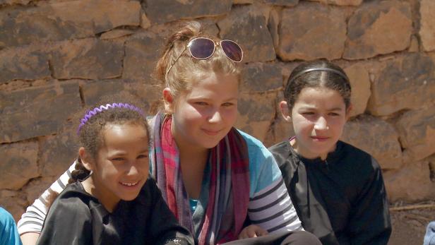 Drei junge Mädchen sitzen vor einer Steinmauer.