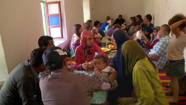 Eine Gruppe von Menschen sitzt in einem Raum und isst gemeinsam Orangen.