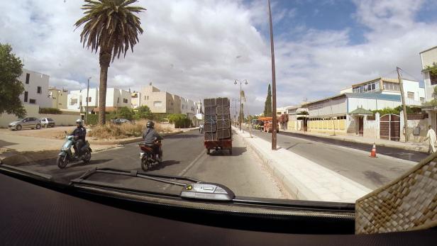 Auf einer Straße in Marokko fahren Motorroller und ein überladener Karren.