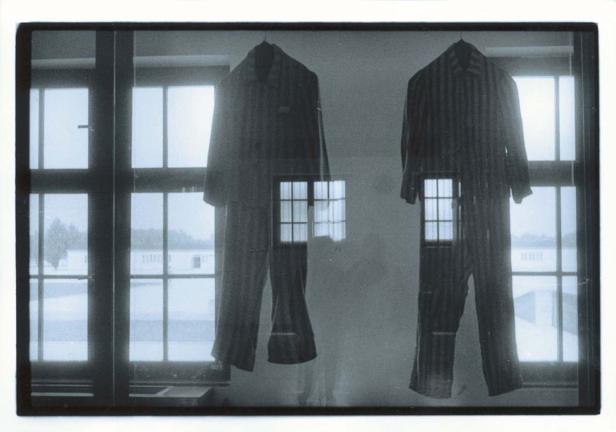 Zwei gestreifte Häftlingsanzüge hängen vor einem Fenster.