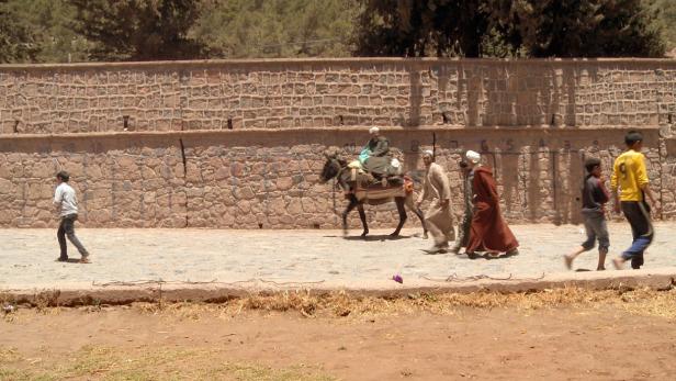 Eine Gruppe von Menschen und ein Mann auf einem Esel gehen an einer Steinmauer entlang.