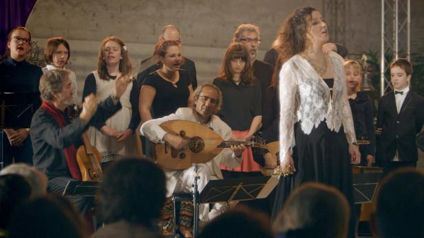 Ein Orchester mit Sängerin, Oud-Spieler und Dirigent tritt vor Publikum auf.