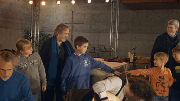 Eine Gruppe von Kindern und Erwachsenen steht auf einer Bühne vor einem Kreuz.