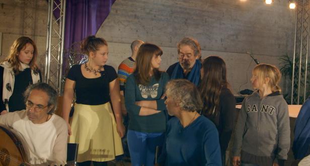 Eine Gruppe von Menschen steht auf einer Bühne, ein Mann spielt ein Saiteninstrument.