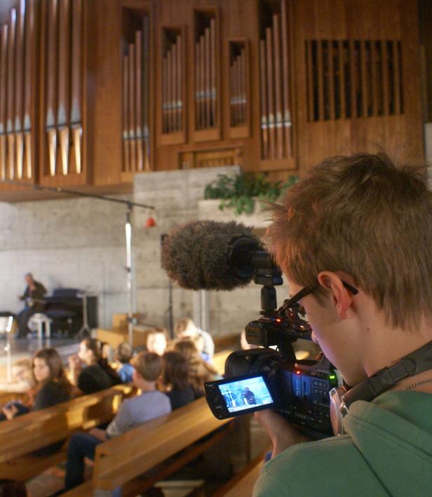 Ein Kameramann filmt eine Aufführung vor einem Publikum in einer Kirche.