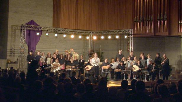 Ein Ensemble spielt auf der Bühne vor Publikum mit Zithern und anderen Instrumenten.