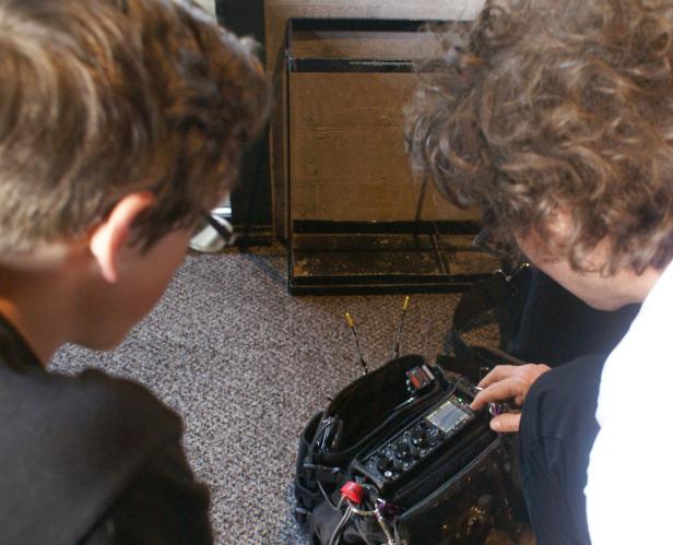 Zwei Personen beugen sich über ein Audiogerät in einer Tasche.