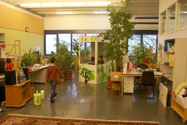 Ein Junge geht durch einen Raum mit vielen Pflanzen und einem Spielhaus.