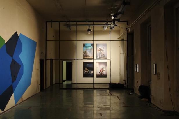 Ein Ausstellungsraum mit vier Bildern an der Wand und einem geometrischen Wandgemälde.