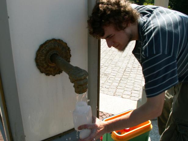 Ein Mann füllt eine weiße Flasche an einem öffentlichen Brunnen.