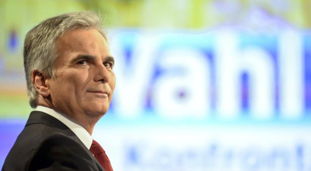 Ein Mann im Anzug steht vor einem Hintergrund mit dem Wort „Wahl“.