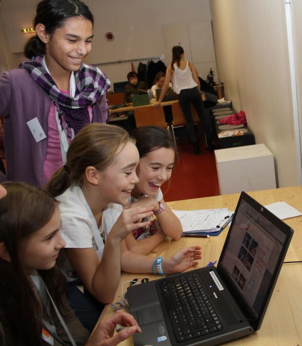 Eine Gruppe Mädchen sitzt an einem Tisch und schaut auf einen Laptop.