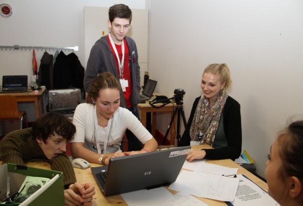 Eine Gruppe junger Leute sitzt an einem Tisch und arbeitet an einem Laptop.