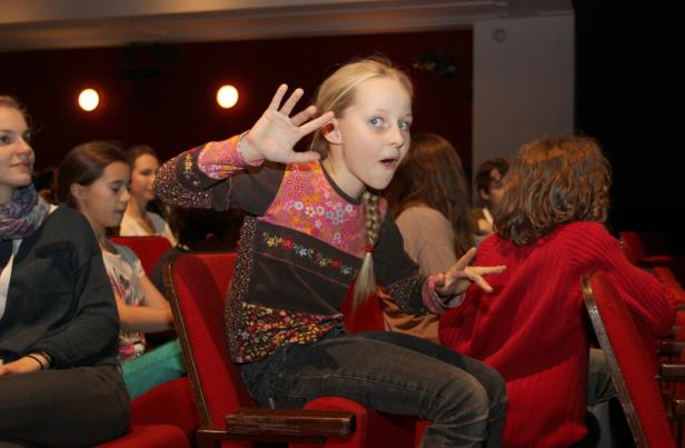 Ein junges Mädchen sitzt aufgeregt in einem Theatersaal.