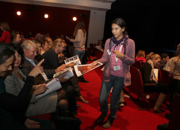 Eine junge Frau verteilt Programmhefte in einem Theatersaal.