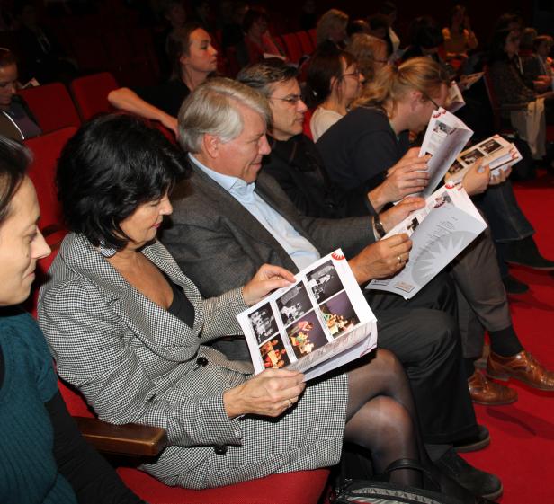 Zuschauer sitzen in einem Theater und lesen Programmhefte.