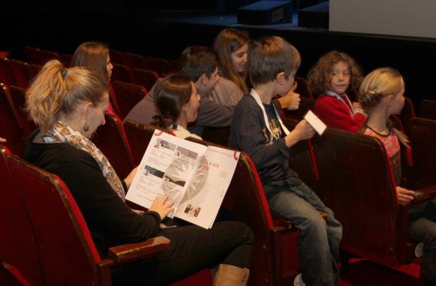 Zuschauer sitzen in einem Theatersaal und lesen Programmhefte.