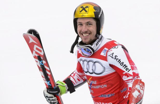 Ein lächelnder Skirennläufer mit Ski und Helm vor einem weißen Hintergrund.