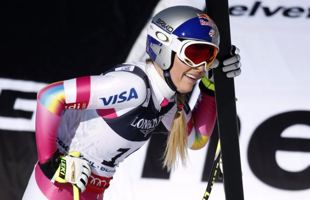 Eine Skirennläuferin mit Helm und Skibrille lächelt und hält ihre Skier.
