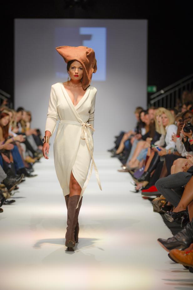 Eine Frau mit Hut präsentiert ein Kleid auf dem Laufsteg.