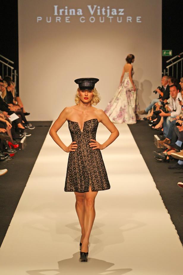 Eine Frau in einem schwarzen Kleid und einer Mütze auf einem Laufsteg.