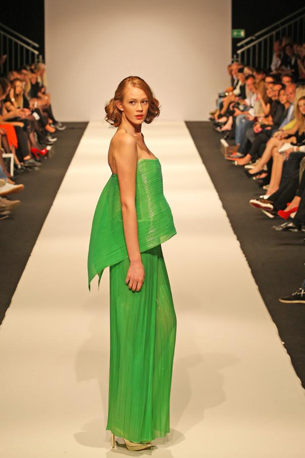 Eine Frau in einem grünen, plissierten Kleid auf einem Laufsteg.